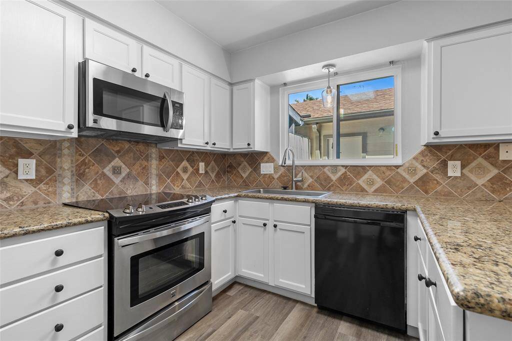 Your kitchen features modern stainless steel appliances, complemented by sleek white cabinetry. The granite countertops and warm, earth-toned tile backsplash add a touch of elegance. A large window above the sink fills the space with plenty of natural light.