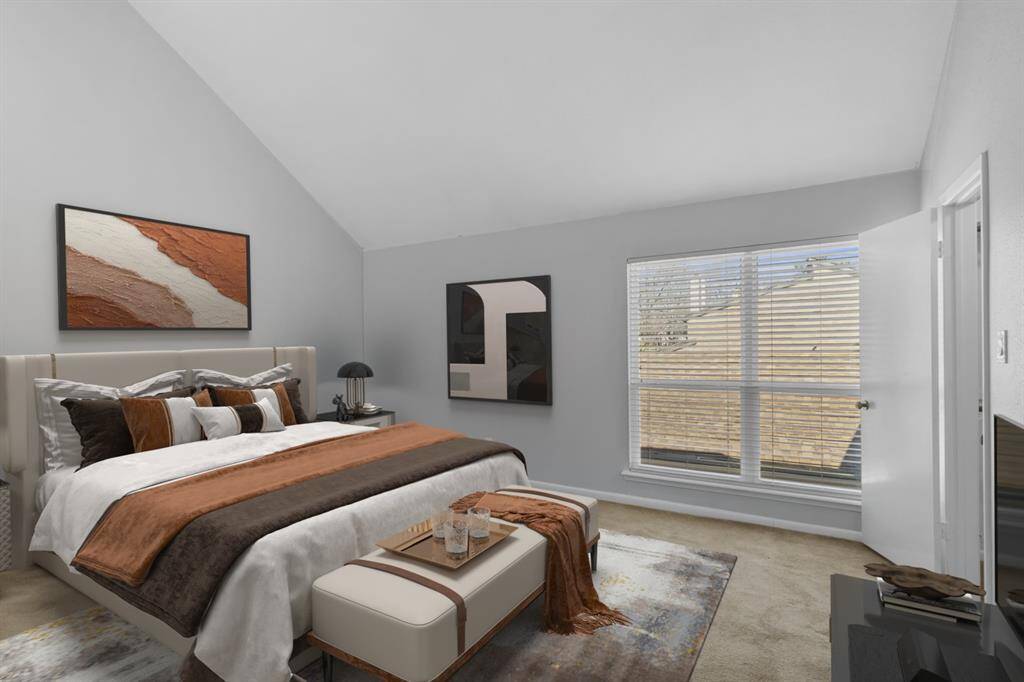 Your spacious primary bedroom offers a peaceful retreat, featuring a vaulted ceiling and abundant natural light streaming through a large window. Soft, neutral tones enhance the calming ambiance, creating a warm and inviting space perfect for relaxation.