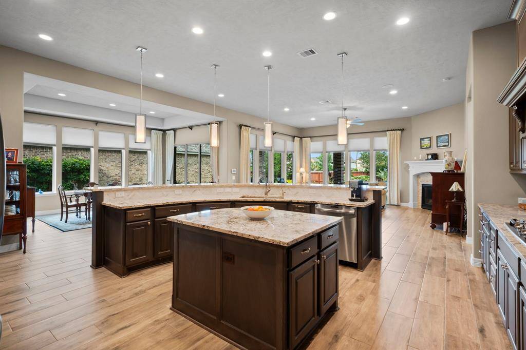 Gourmet chefs and home cooks alike will be inspired in this spacious kitchen, showcasing elegant wood-look  tile flooring. Sleek granite countertops, recessed lighting, and stainless steel appliances add modern style. At the heart of the kitchen lies a thoughtfully designed island, offering both beauty and function. With additional storage, open shelving, and a gracefully curved edge that mirrors the peninsula, it provides ample prep space for the avid home chef.