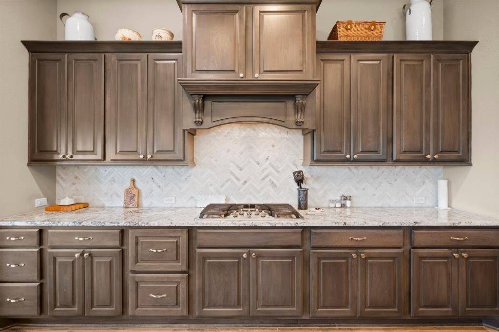 Thoughtful features like a pull-out trash/recycle drawer and deep drawers for pots and pans enhance functionality, while the furniture quality vent hood showcases both warmth and quality. A sophisticated herringbone tile backsplash adds visual interest, and the generous walk-in pantry provides outstanding storage.