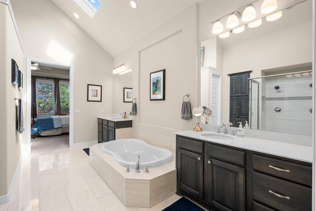 The spa-inspired bath features dual vanities, each set apart from the other to provide ample personal space and privacy. Rich cabinetry is complemented by gleaming granite countertops, under-mount sinks, and generously-sized mirrors, creating a harmonious blend of elegance and function. A striking art niche above the soaking tub adds a designer touch, making this serene space as visually stunning as it is practical.