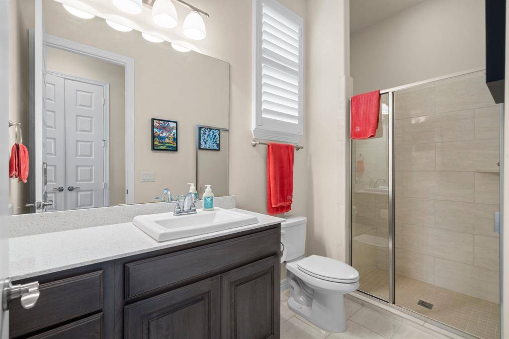 The en-suite bathroom for Bedroom 2 includes single sink with extended granite countertop, rectangular tile flooring, sunny window, hall linen closet, toilet, and tiled shower with bench seat and toiletry shelf.