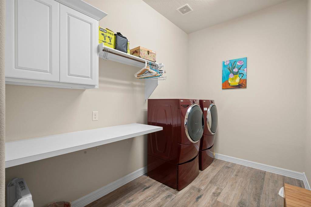 Utility room is conveniently located for easy laundry time! It has a mud area outside by the garage entrance with an organization system for the busy family.  The laundry room features wood-look tile flooring, upper cabinet for storage, and a folding counter. There is also plenty of space to remove the folding counter and add a second refrigerator if desired.