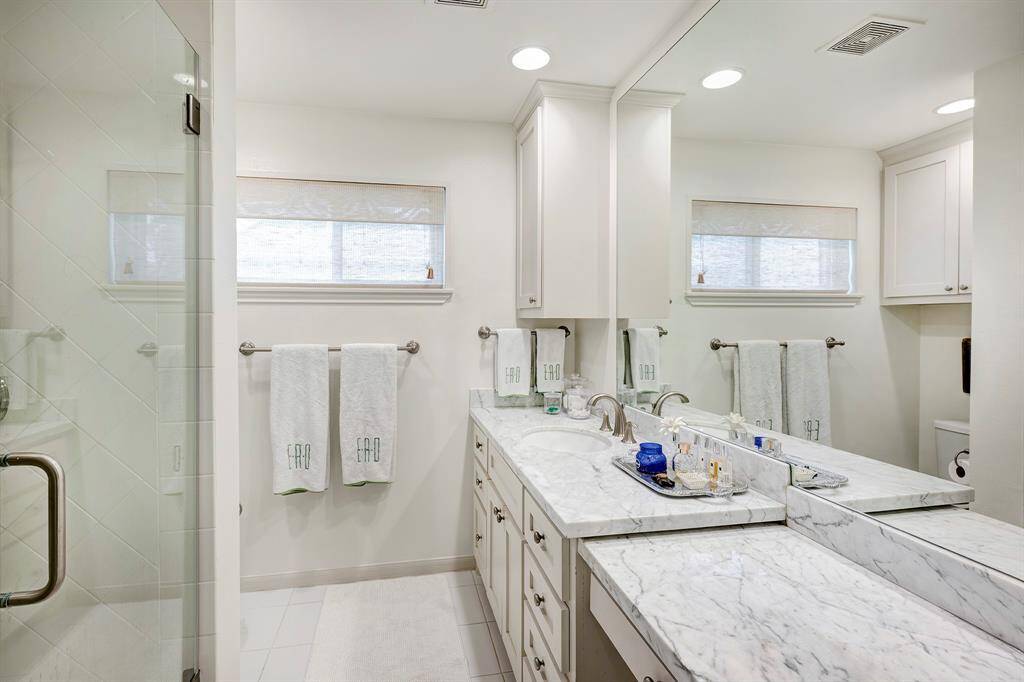 Primary bath with a glass-enclosed shower, timeless neutral tile, plenty of counter space, large mirror, and ample storage.