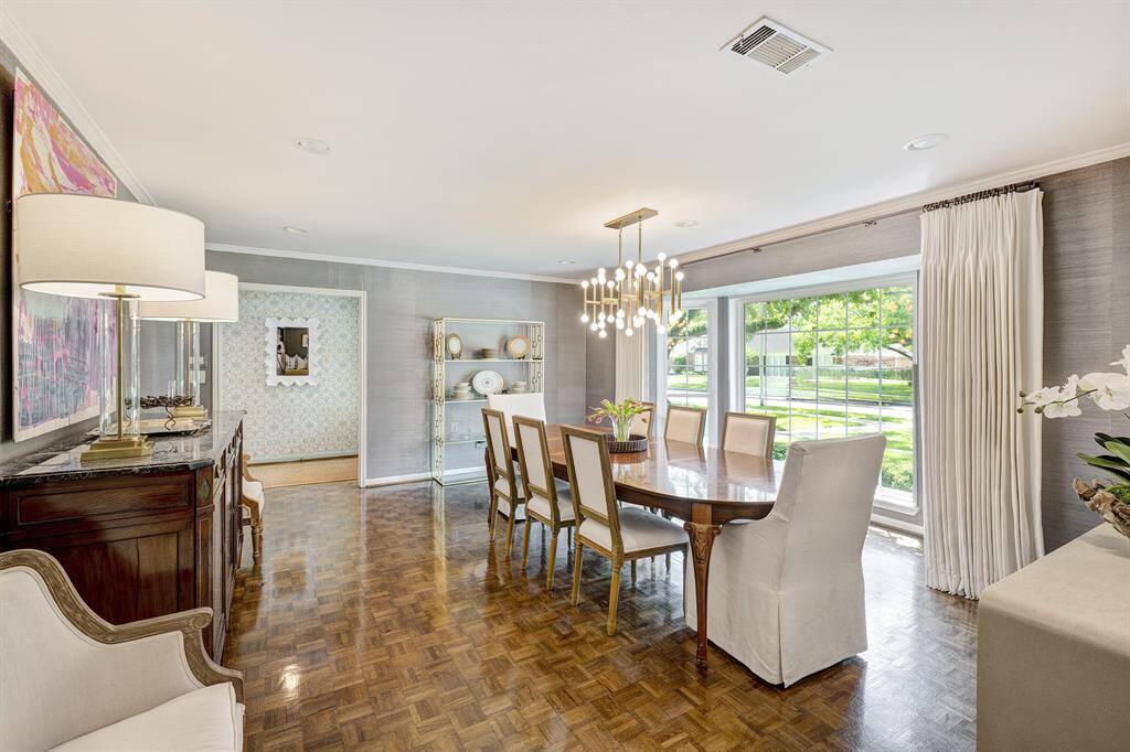 Spacious and elegant dining room featuring classic parquet floors, an updated chandelier, and a large window with a view of the front yard.