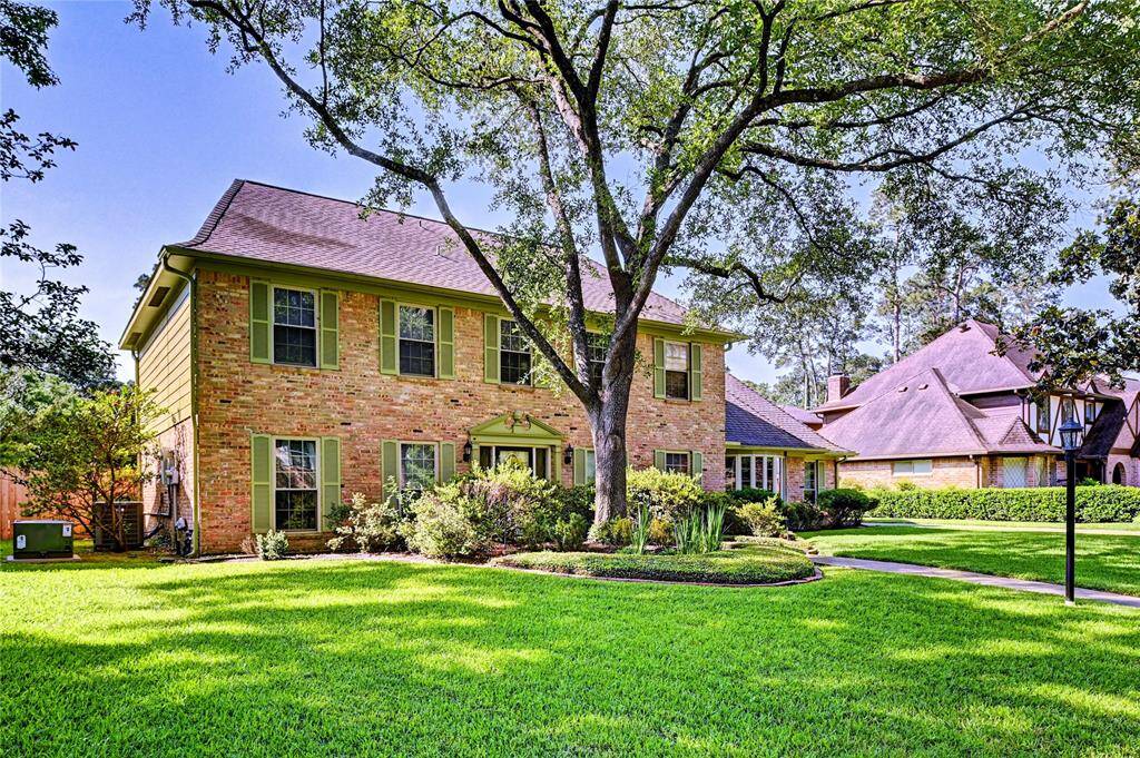 This charming two-story brick home features a well-maintained front yard with lush green grass and mature trees, offering ample shade. The traditional architecture is complemented by numerous windows, allowing plenty of natural light inside. A curved walkway leads to the front entrance, adding to its welcoming appeal.
