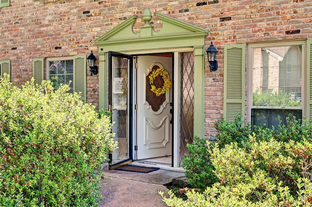 Charming brick exterior with inviting greenery and a welcoming front door, featuring decorative glass and a wreath. Classic shutters and lantern-style lighting add elegance.