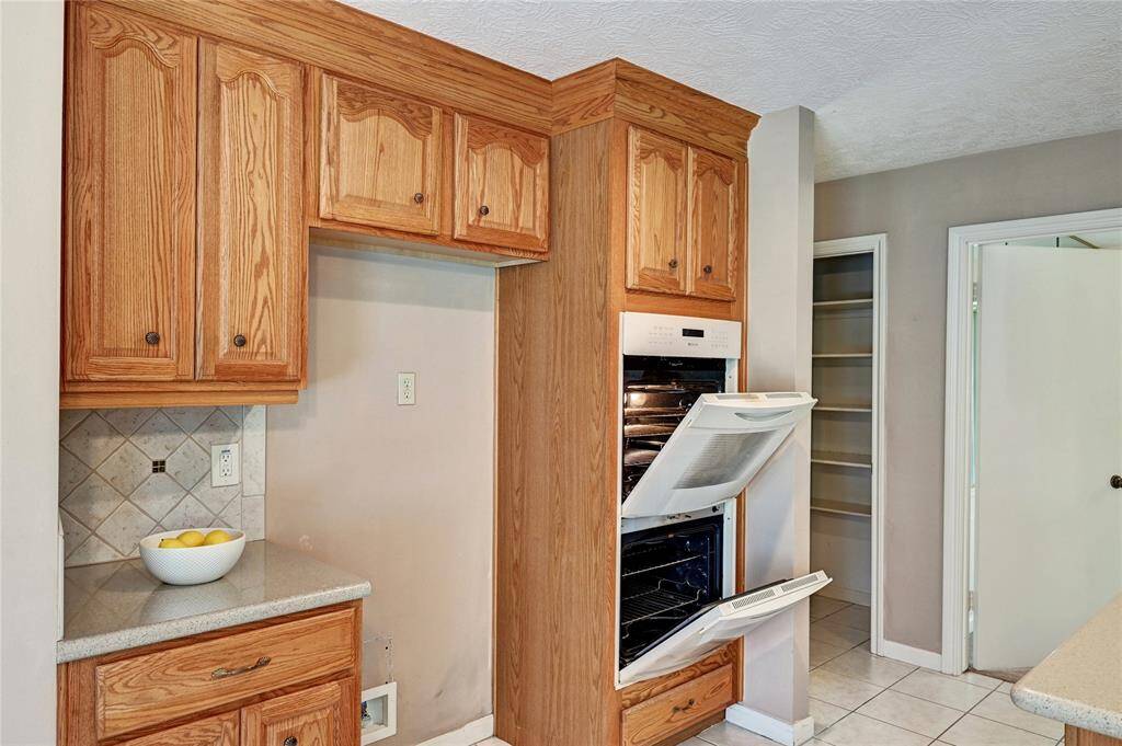 This kitchen features warm wooden cabinetry, a built-in double oven, and tile countertops. The space includes a small pantry area and a neutral tile backsplash, offering functionality and a classic look.