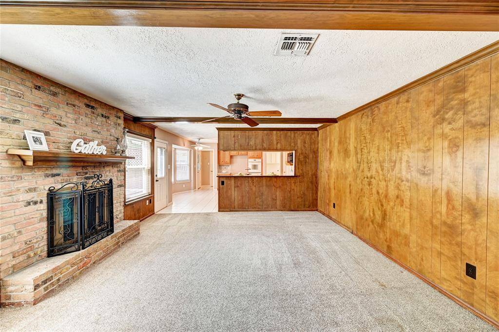 This cozy living area features a brick fireplace with a mantel, wood-paneled walls, and a ceiling fan. It opens up to a bright kitchen with a pass-through window, ideal for entertaining and family gatherings.