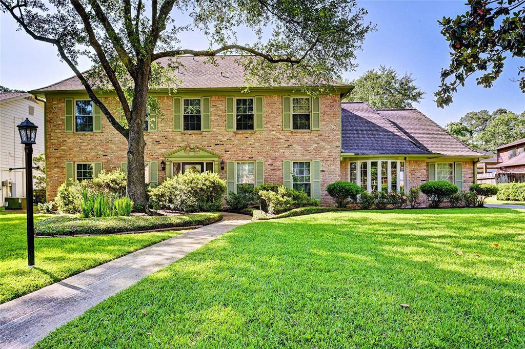This charming two-story brick home features a well-maintained lawn, mature trees, and classic green shutters. A welcoming pathway leads to the front entrance, surrounded by lush landscaping. Perfect for those seeking a traditional and inviting exterior.