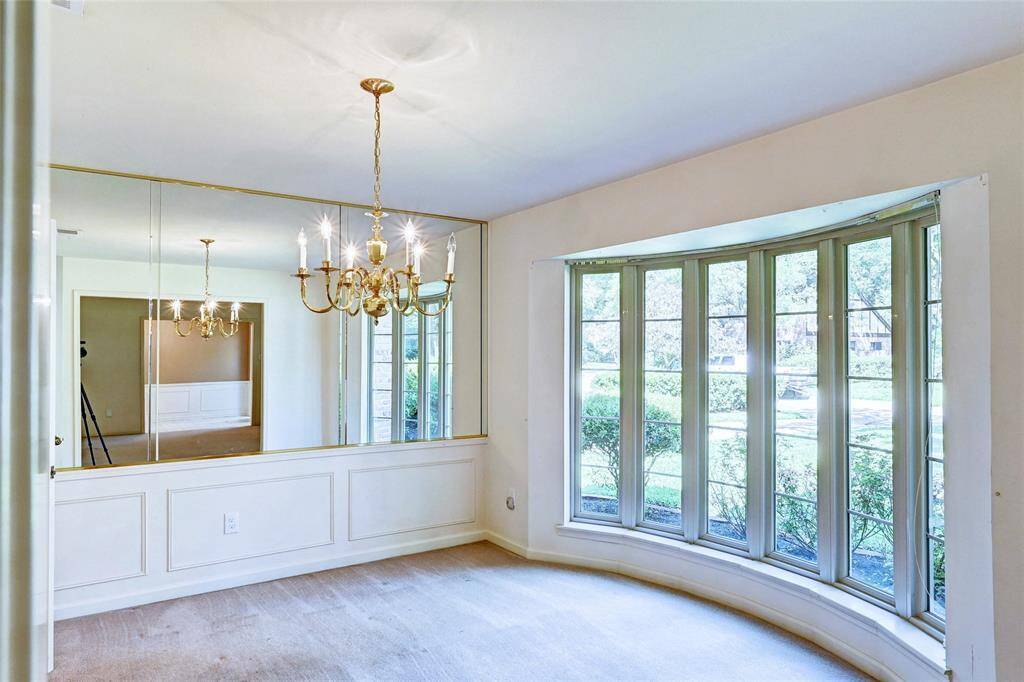 This room features a large bay window offering ample natural light and a view of the garden. It has a mirrored wall that enhances the sense of space and a classic chandelier adding elegance.
