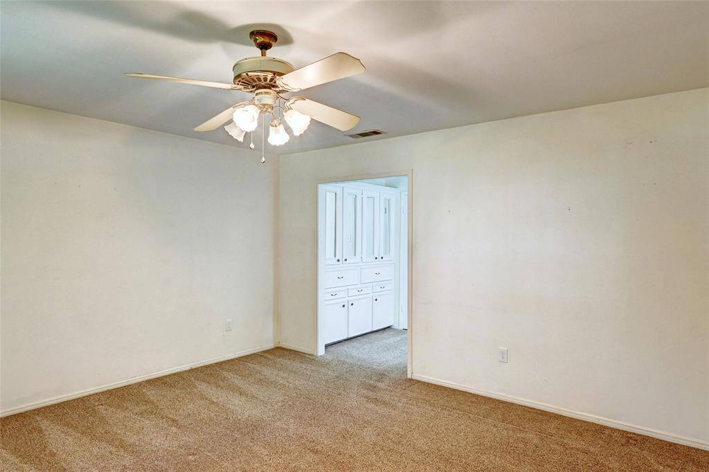 This room features neutral walls, carpet flooring, and a ceiling fan with lights. It connects to the primary bathroom with built-in white cabinetry, offering potential for versatile use.