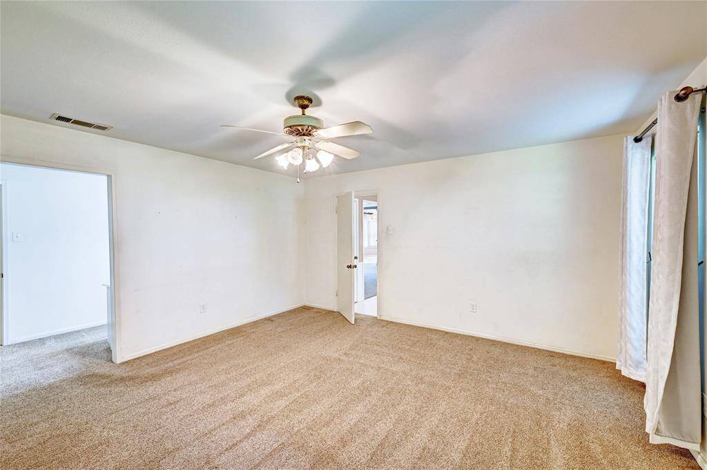 This primary bedroom features neutral carpet and walls, a ceiling fan with lights, and ample natural light offering a spacious and versatile layout.