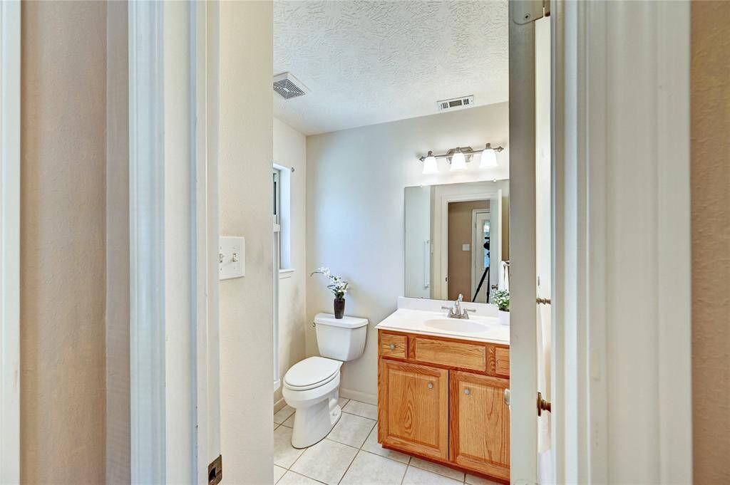 Bright half bathroom with neutral tones, featuring a single vanity, large mirror, modern light fixture, and tile flooring.
