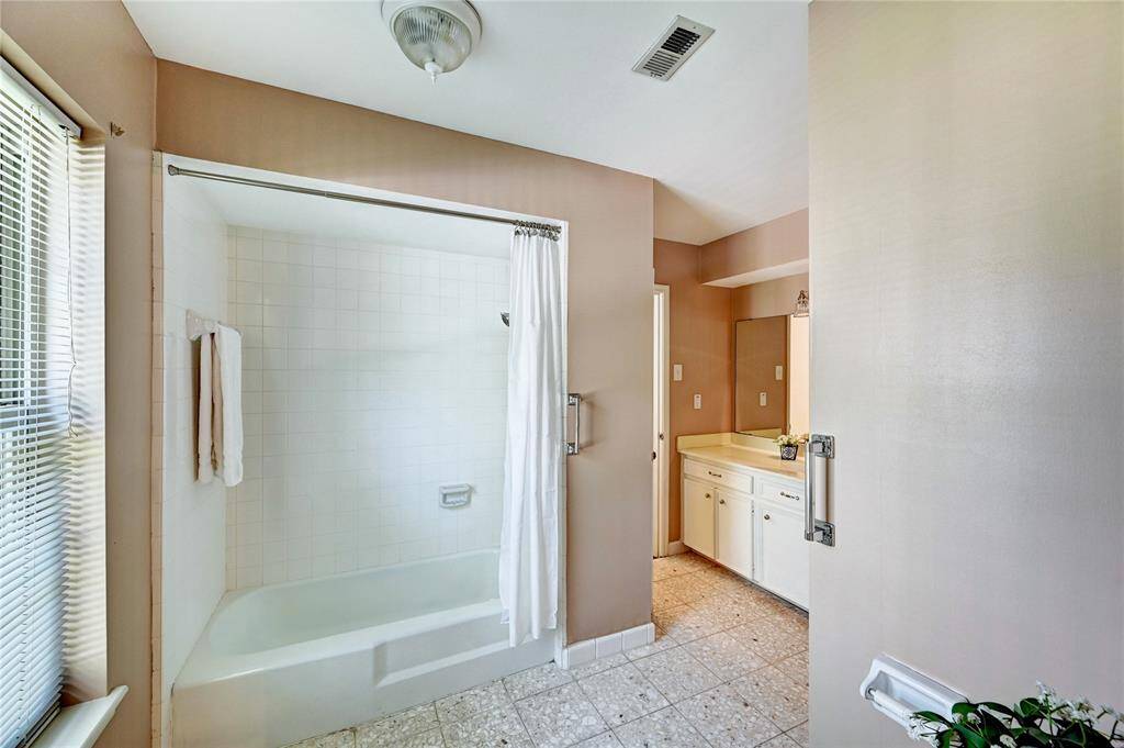 A bright bathroom featuring a shower-tub combo, a large vanity with a mirror, and natural light from a window. The space has neutral tones and functional fixtures.