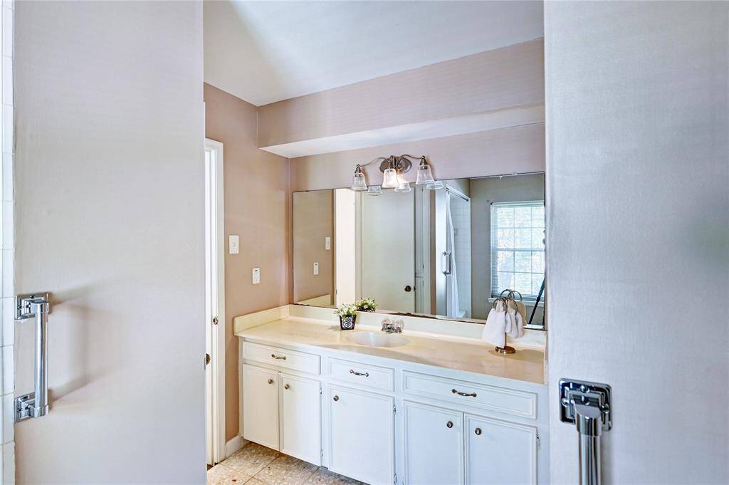 This bathroom features a spacious vanity with ample counter space and storage, a large mirror, and stylish lighting. It has a clean, bright look with natural light coming through a window.