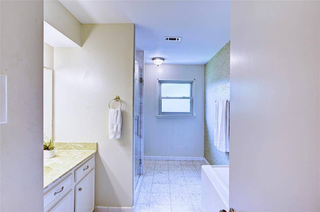 Bright bathroom with a large countertop, a window for natural light, and a separate remodeled shower area. Neutral tones create a clean, spacious feel.
