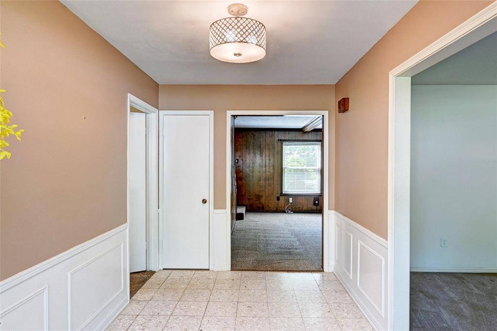 Hallway with tiled flooring, beige walls, and white wainscoting. A modern ceiling light fixture adds a touch of elegance.