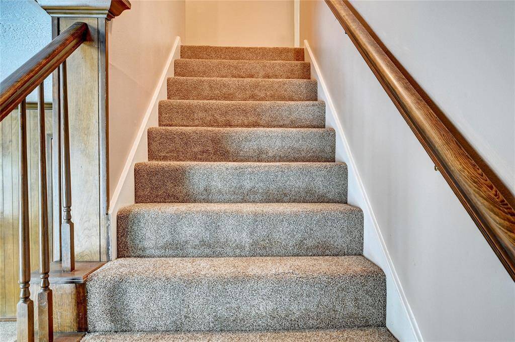 Carpeted staircase with wooden handrails on both sides, leading to the upper floor, offering a cozy and inviting transition between levels.