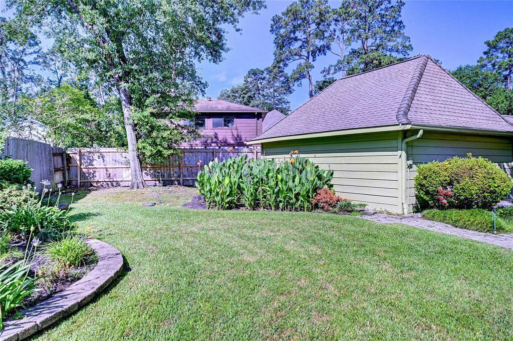 This backyard features a well-maintained lawn with lush greenery and a variety of plants. A wooden fence provides privacy, and a detached garage is adjacent, offering practical storage or parking space. The area is peaceful and inviting, perfect for outdoor activities or relaxation.
