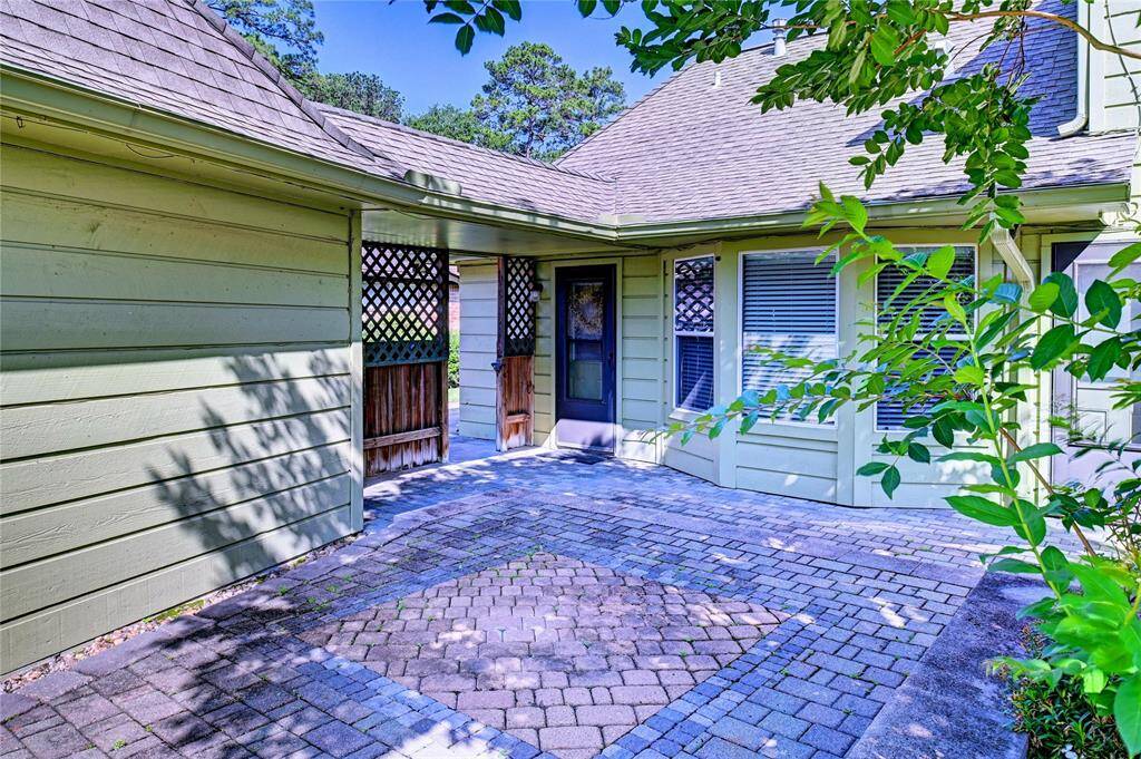 Charming exterior with a cozy courtyard feel, featuring a paved patio and greenery. The house has a warm, inviting green siding and lattice accents, ideal for enjoying outdoor relaxation.