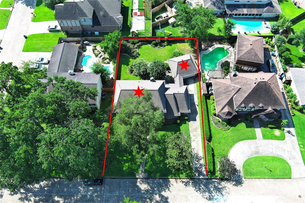 This aerial view showcases this spacious property which is outlined in red, featuring a well-maintained home with a large front yard and abundant greenery. It is situated in a desirable residential area.
