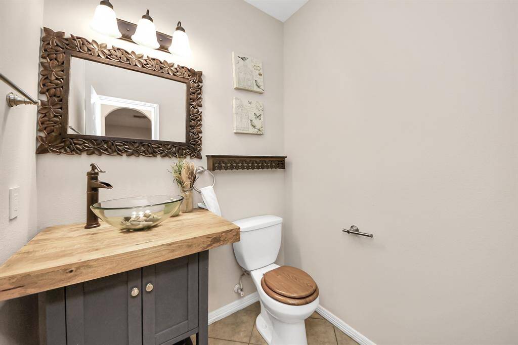 This bathroom features a rustic wooden vanity with a stylish glass vessel sink, a decorative framed mirror, and modern lighting.