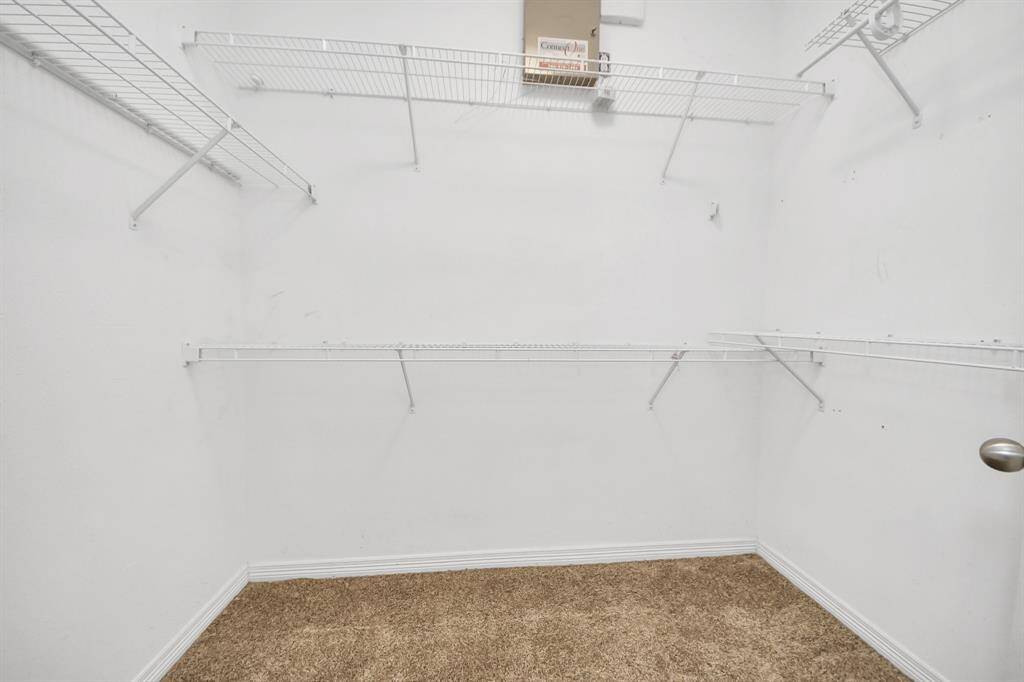Spacious walk-in closet with white wire shelving on three walls and carpeted flooring, ideal for ample storage.