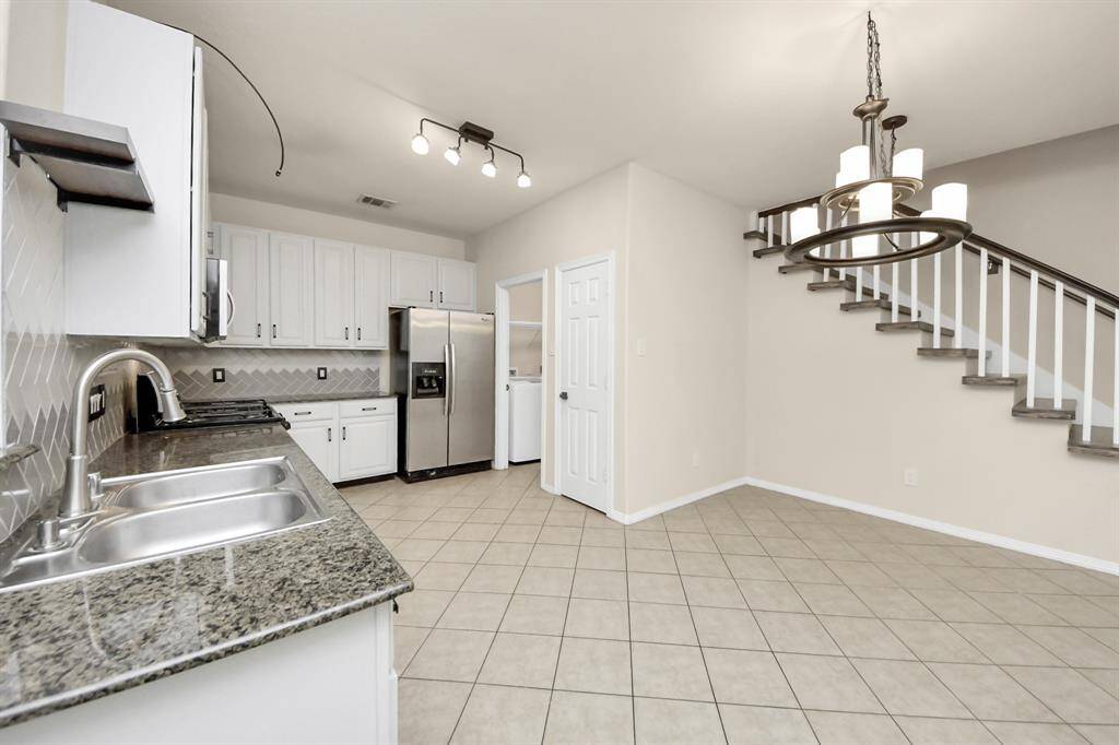 Bright kitchen with granite countertops, stainless steel appliances, and tile flooring. Features a modern light fixture and adjacent dining area.