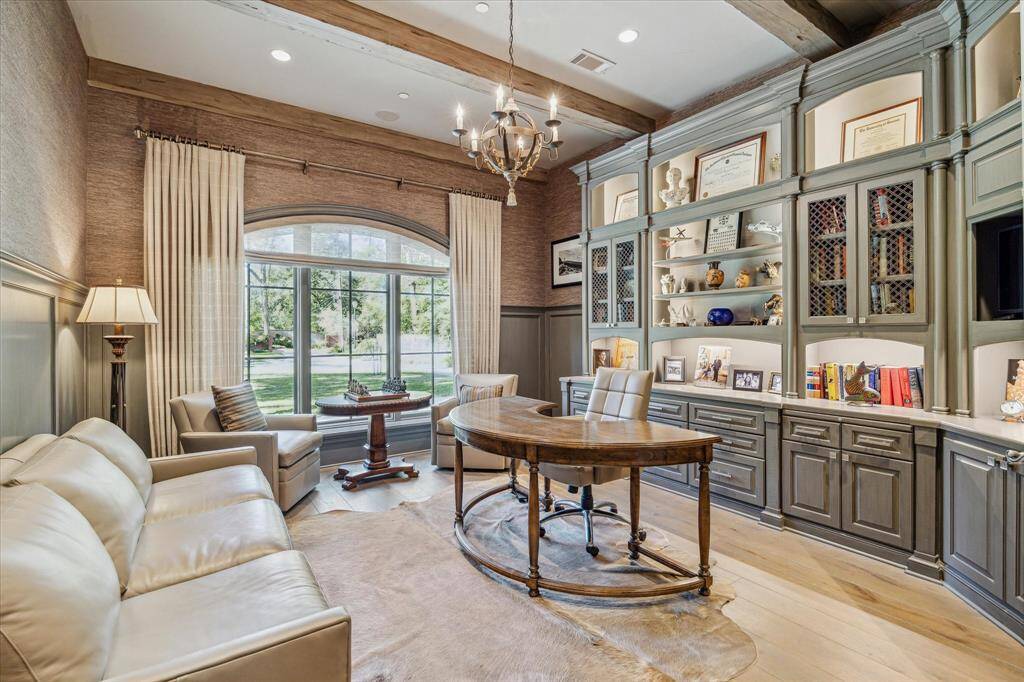 The handsome study is complete with beamed ceiling, modern wallpaper, lighted cabinetry and custom draperies.