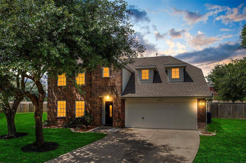 This charming two-story brick home features a spacious front yard with mature trees, a two-car garage, and well-lit windows. The inviting facade combines classic and modern elements, perfect for family living.
