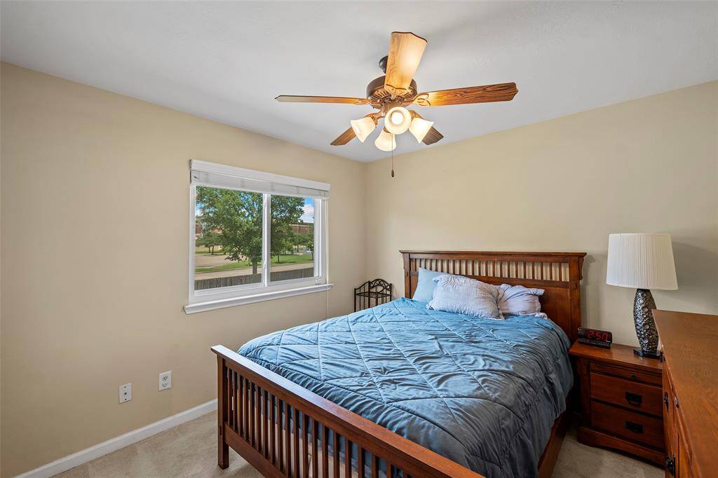 Cozy bedroom with neutral walls, featuring natural light and windows in each bedroom. A ceiling fan provides comfort, and a window offers natural light and a view of the outdoors.
