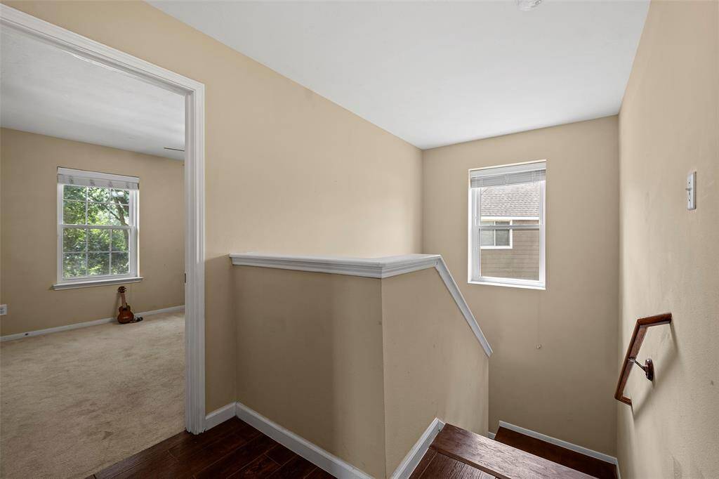 Bright and welcoming upstairs landing with neutral walls, hardwood floors, and natural light from two windows.