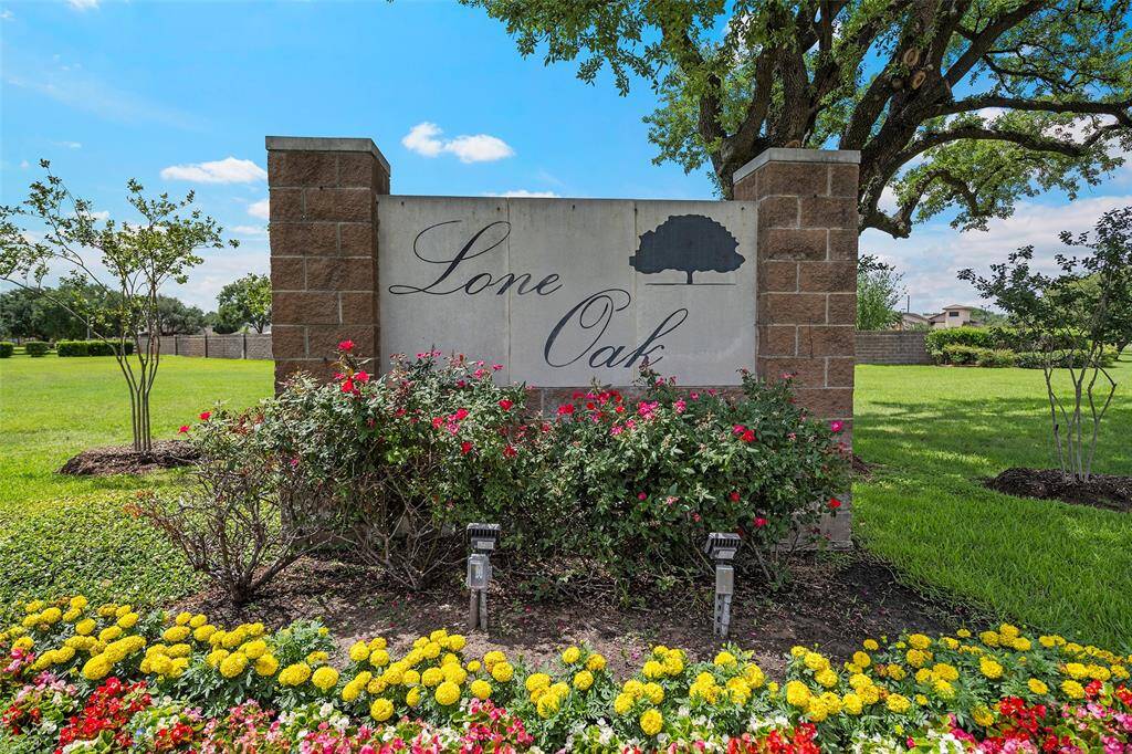 Entrance to "Lone Oak" featuring a well-maintained sign surrounded by vibrant flowers and lush greenery, indicating a welcoming and attractive neighborhood setting.