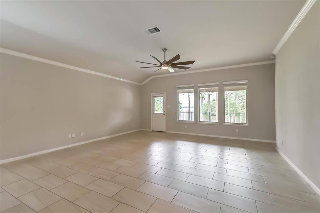 Large living room with crown molding, tile flooring, fan and picture windows
