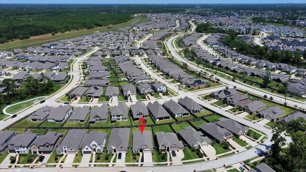 Aerial view of a large suburban neighborhood with rows of single-family homes featuring well-maintained lawns and driveways. The area is surrounded by greenery and has a mix of winding and straight streets, offering a spacious and organized community layout.