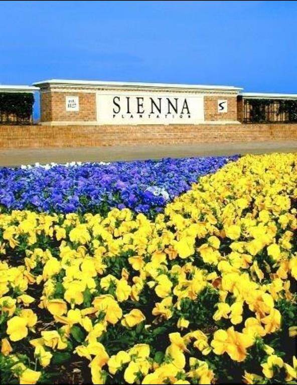 This photo showcases the entrance to Sienna Plantation, featuring a brick sign with vibrant yellow and purple flowers in the foreground, creating an inviting and colorful welcome.