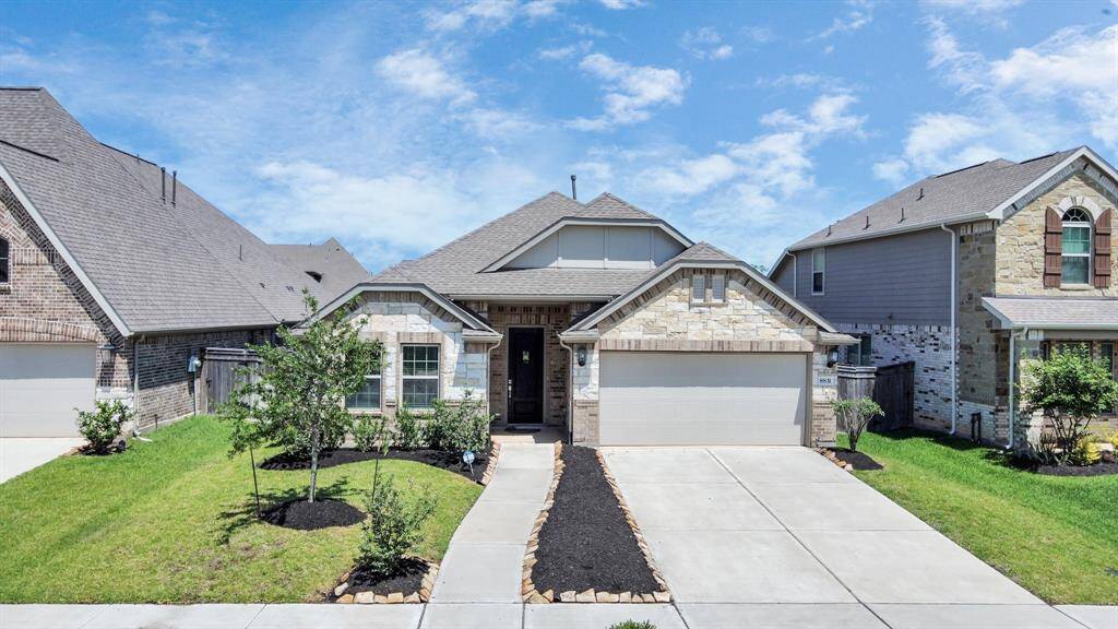 Charming single-story home with a stone façade and a two-car garage. It features a well-maintained front yard with young trees and shrubs, and a clean, inviting driveway. Located in a neighborhood with similar style houses.