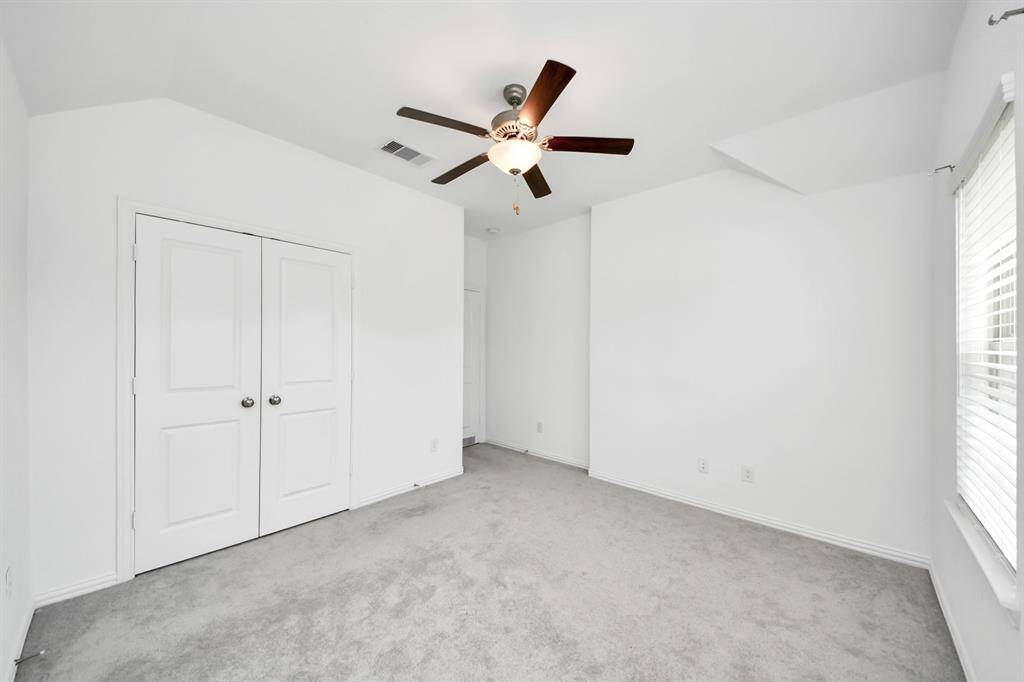 Spacious and bright bedroom featuring plush carpeting, a ceiling fan, and ample closet space, perfect for relaxation and comfort.