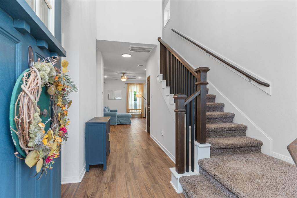 Welcome home! This bright and welcoming entryway sets the tone with warm wood-look floors, soaring ceilings, and a beautifully crafted staircase. Natural light pours in, creating a fresh, airy feel as you step inside. A cozy living space awaits just beyond, perfect for relaxing or entertaining