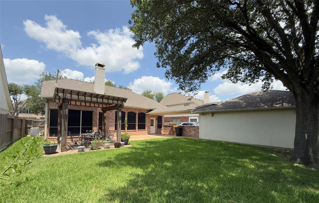 Spacious backyard with a well-maintained lawn, a large tree providing shade, and a covered patio perfect for outdoor seating. The brick exterior adds charm, and there’s ample space for gardening.