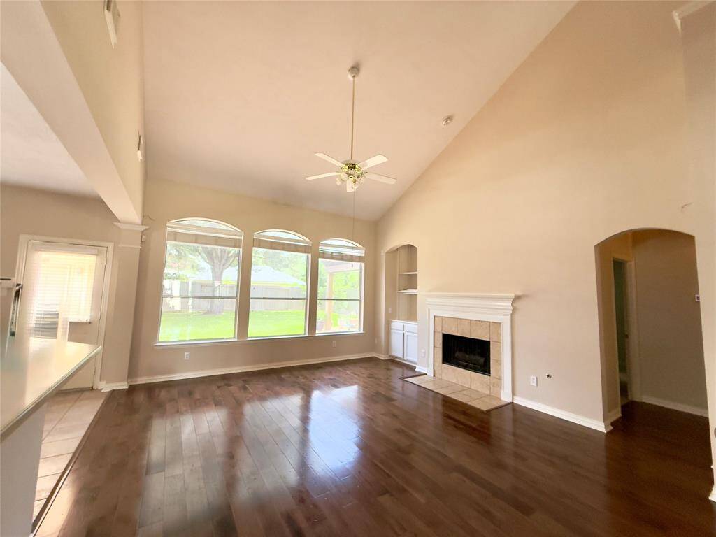 Bright and spacious living room with high ceilings, large windows, hardwood floors, and a cozy fireplace. The space opens to a kitchen area, providing a great flow for entertaining.