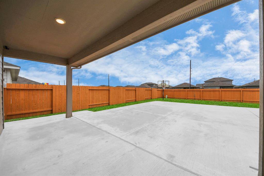 This photo showcases a spacious backyard with a large concrete patio, perfect for outdoor activities and entertaining. The area is enclosed by a wooden fence, providing privacy and a basketball hoop for recreation.