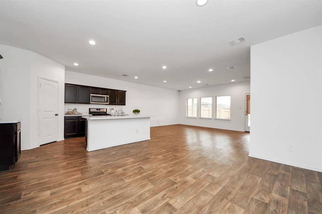This spacious open-concept living area features hardwood floors, recessed lighting, and a modern kitchen with dark cabinets and a large island. Ample natural light from multiple windows enhances the airy feel, making it ideal for entertaining.