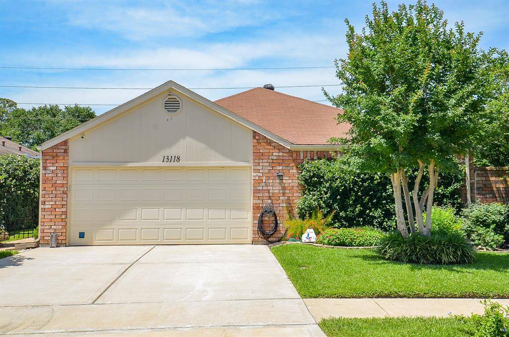 This photo showcases a single-story brick home with a two-car garage. The front yard is well-maintained, featuring a lush green lawn, neatly trimmed bushes, and a mature tree. The driveway is spacious and clean, leading up to the garage.