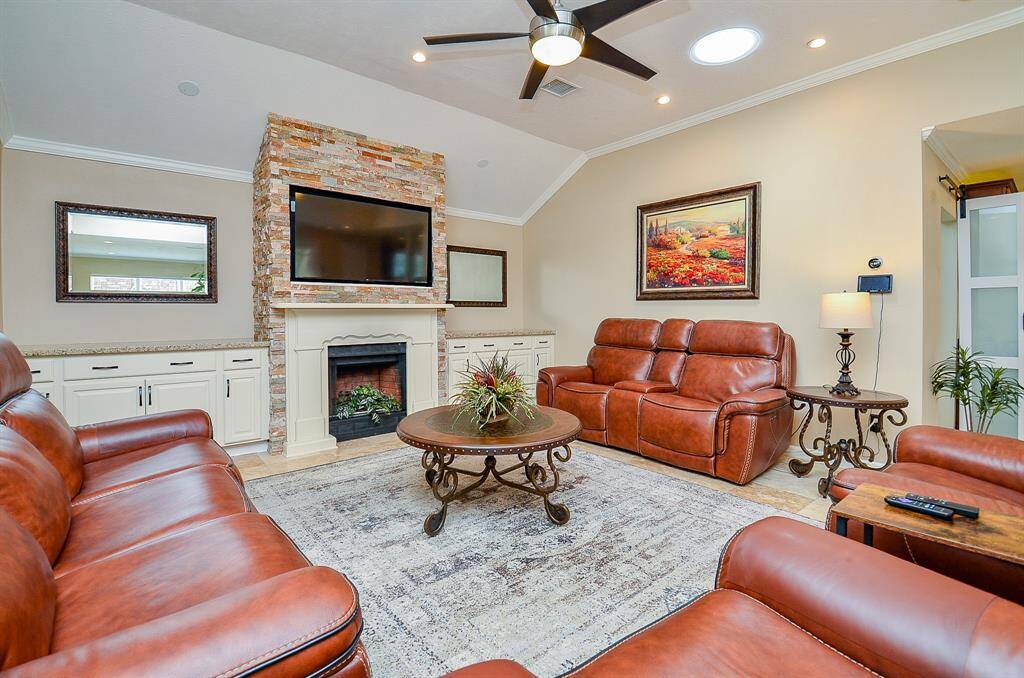 Large living room features a stone fireplace and a ready mount for a TV. The room is well-lit with a ceiling fan, recessed lighting, and a skylight. Built-in cabinets offer wonderful storage