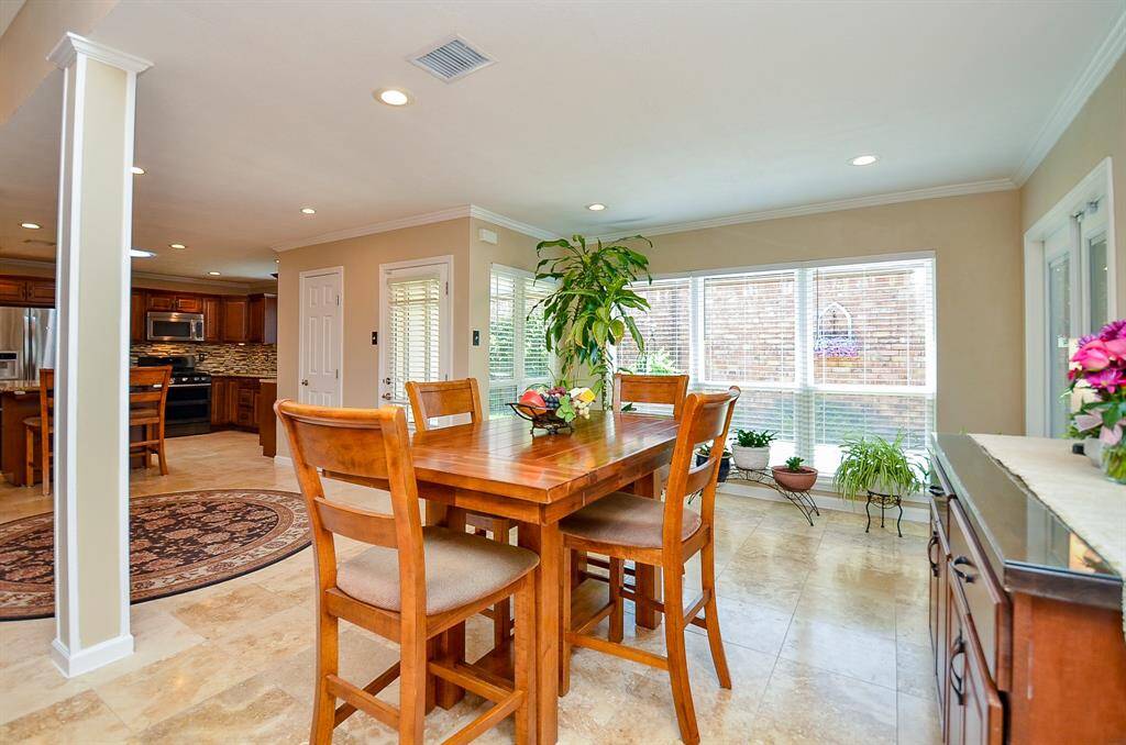 Bright and inviting dining area with a wooden table set, large windows offering ample natural light, and a view into a modern kitchen with stainless steel appliances. Perfect for family gatherings.