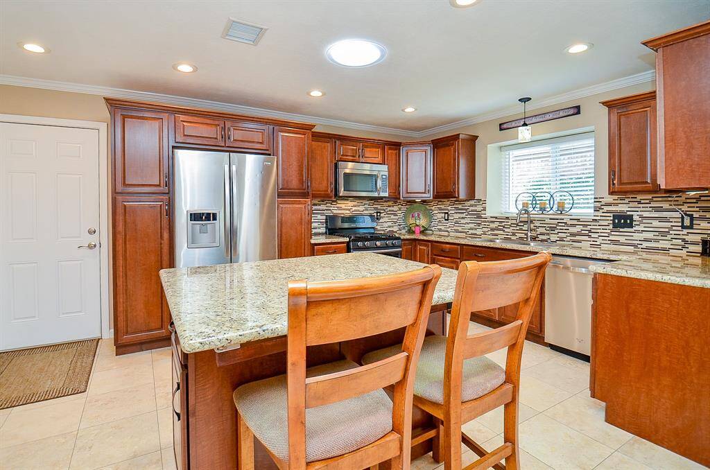 Light and open  kitchen features elegant wood cabinetry, granite countertops, and a stylish tile backsplash. It includes stainless steel appliances, a central island with seating, and recessed lighting, creating a bright and inviting space.
