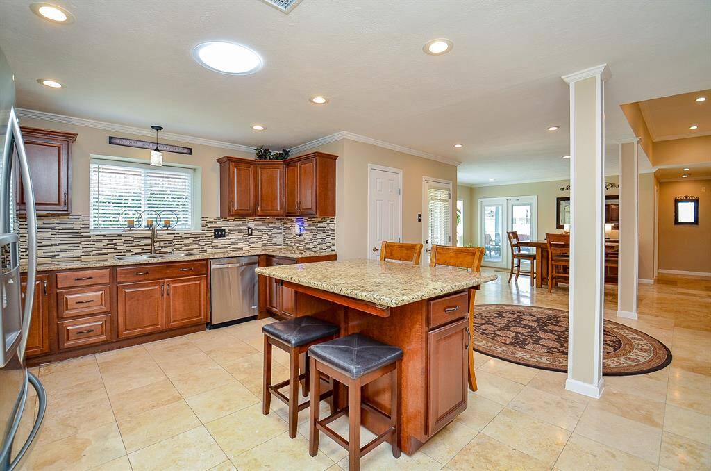 Spacious kitchen features elegant wooden cabinets, a stylish tile backsplash, and a central island designed for in kitchen seating. The open floor plan extends to a dining area, enhancing the home's airy feel.