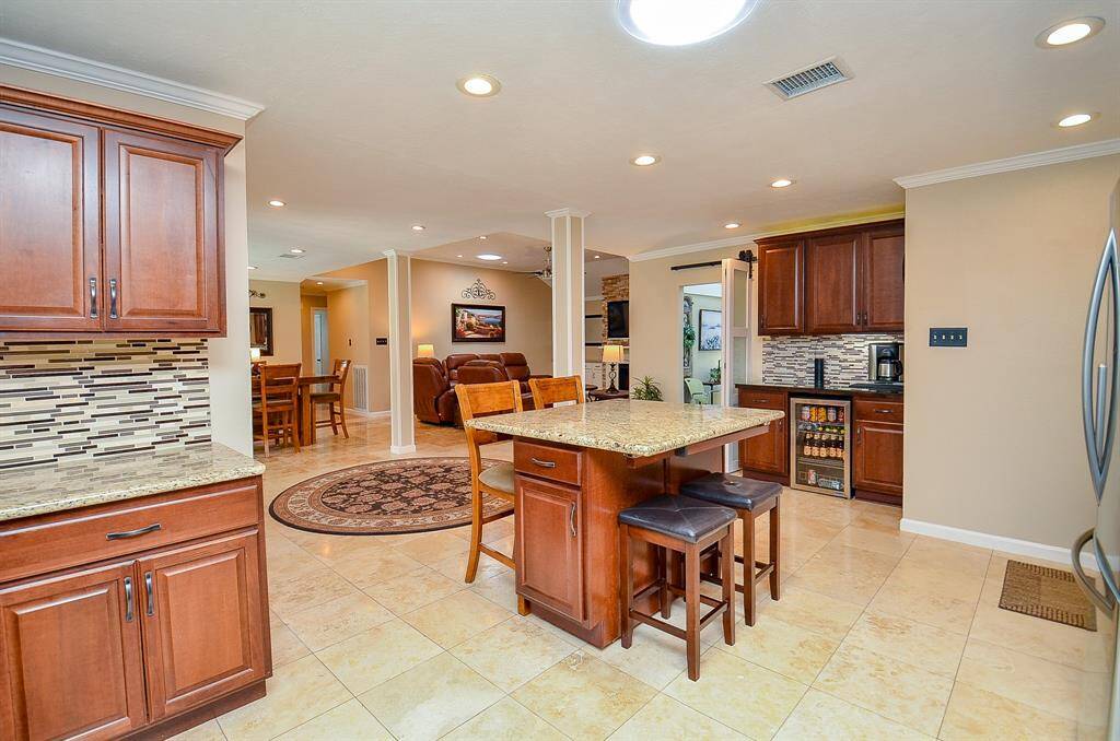 Open-concept kitchen features elegant wood cabinetry, granite countertops, and a central island with seating. The kitchen seamlessly flows into a cozy living area, with warm lighting and a contemporary design. Perfect for entertaining and family gatherings.